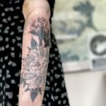 A woman’s forearm, with a fine line black and grey Japanese style tattoo of a peony. Floral tattoo by tattoo artist Harriet Street