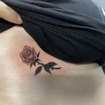 Tiny, black and grey, fine line rose, tattooed on the side of a woman's ribes, just under her breast line by Harriet Street at Cult Classic Tattoo